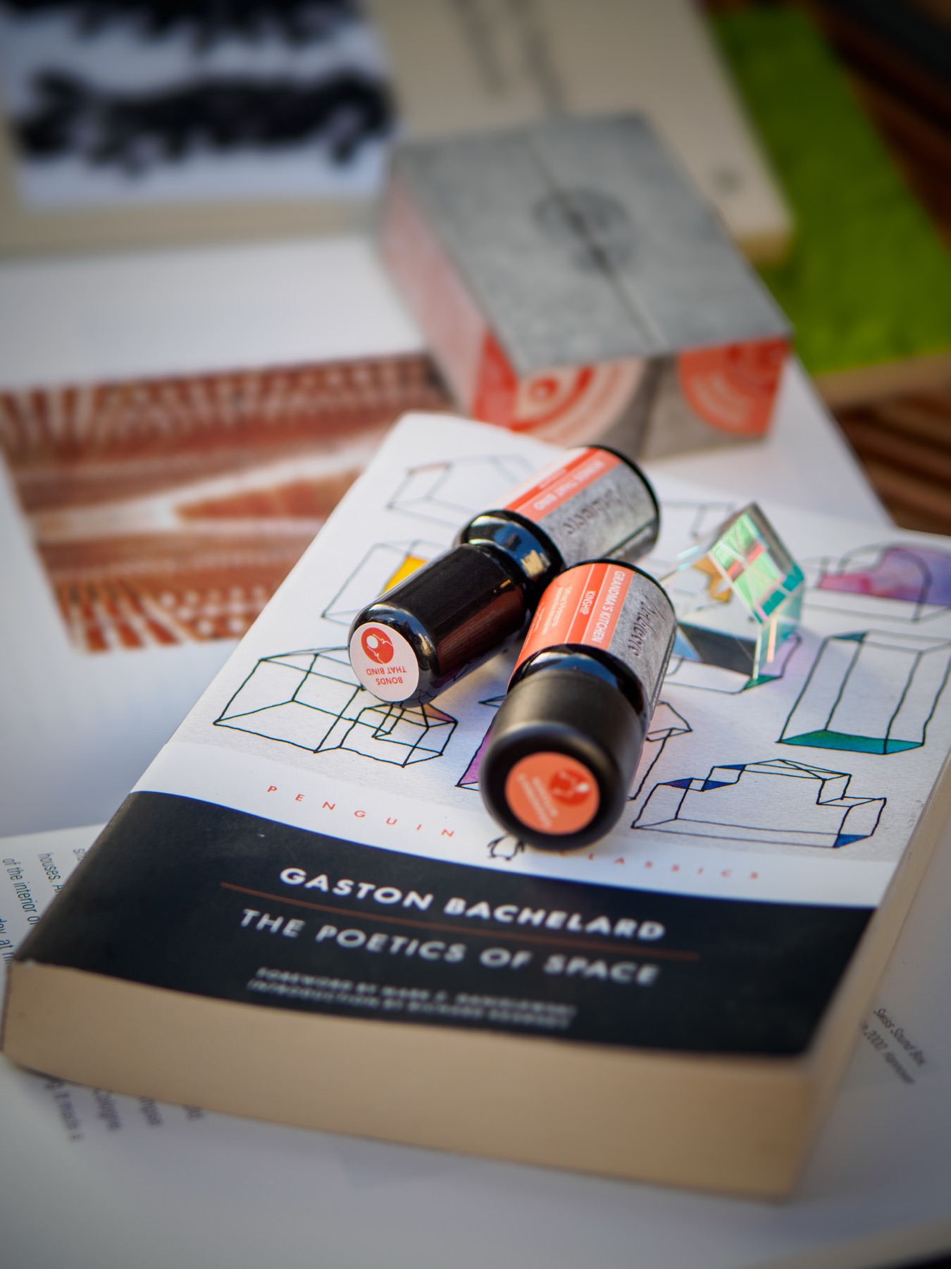 Two small essential oil bottles and a glass house resting on a copy of The Poetics of Space by Gaston Bachelard.
