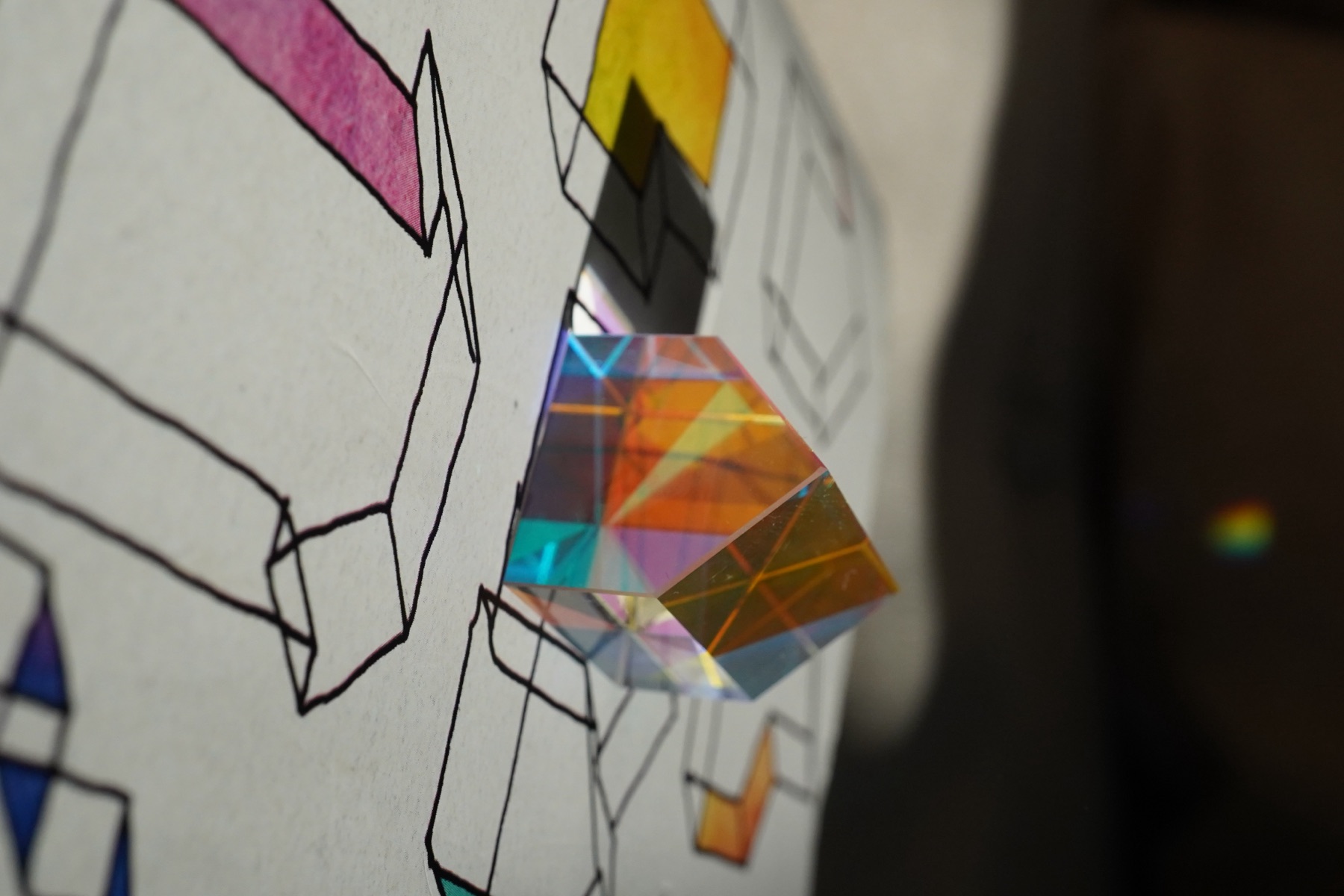 A glass house standing on a sheet of hand-drawn houses, some filled with colour.